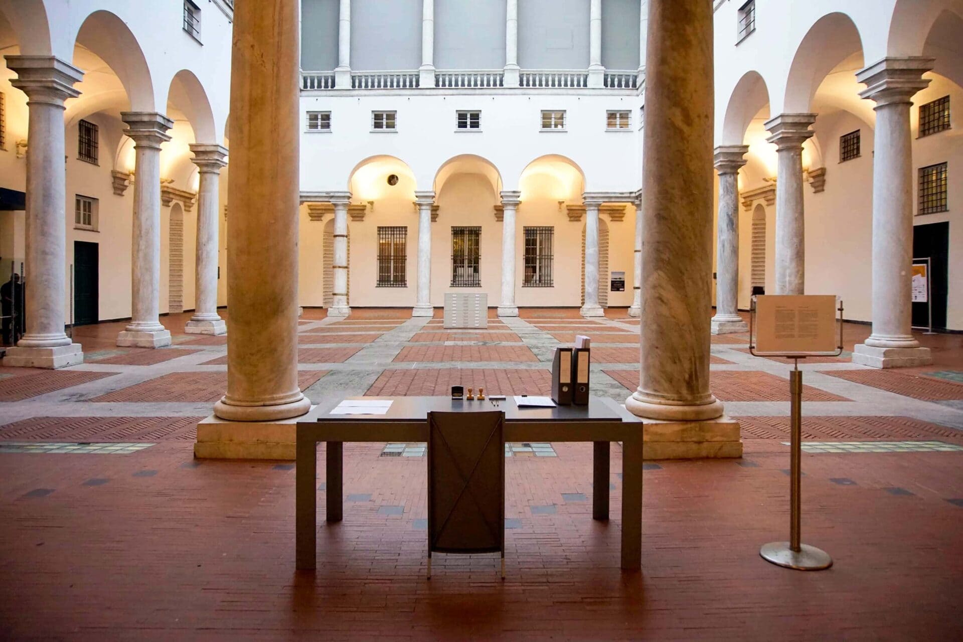 Patricia Sandonis artistic installation at Palazzo Ducale, showing a desk, a chair and folders in the courtyard