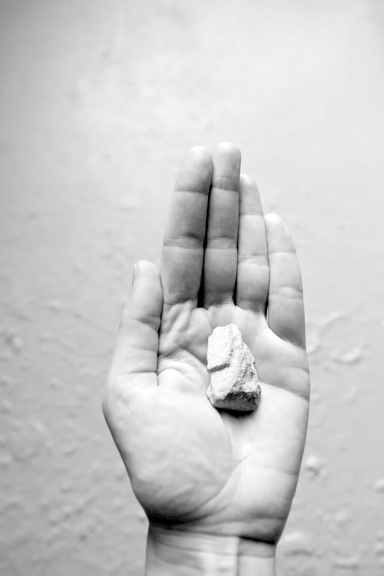 Black and white photography showing a left hand with a small stone