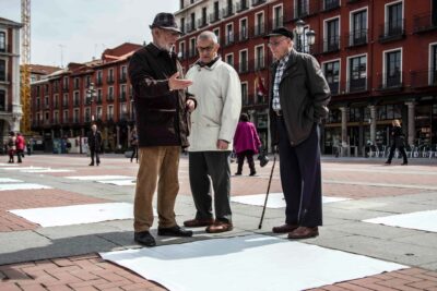 Three old men talking and participating in Patricia Sandonis large-scale art installation in Plaza Mayor de Valladolid