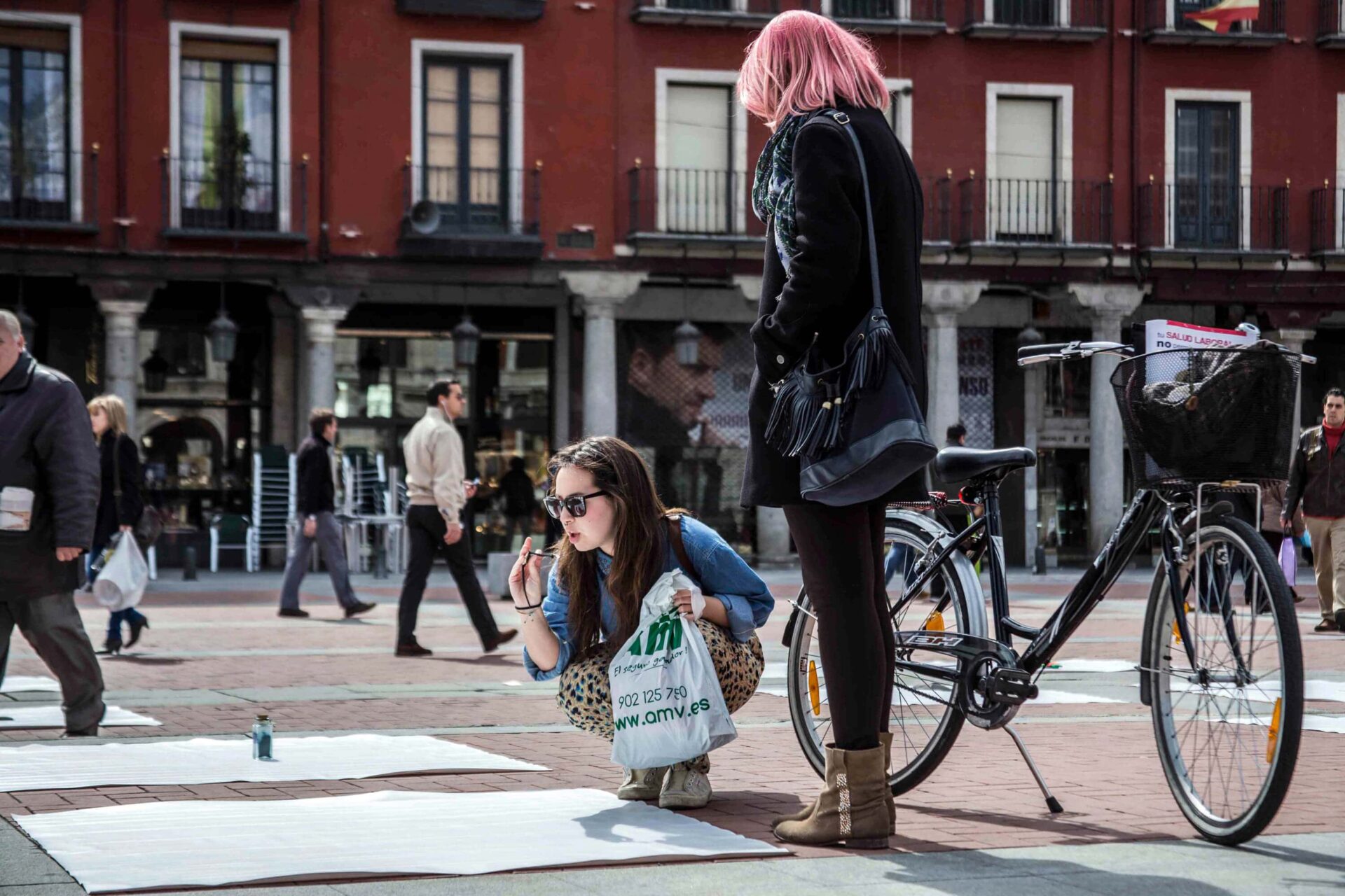 Two women with a bike and a plastic bag participating in Patricia Sandonis large-scale art installation in Plaza Mayor de Valladolid