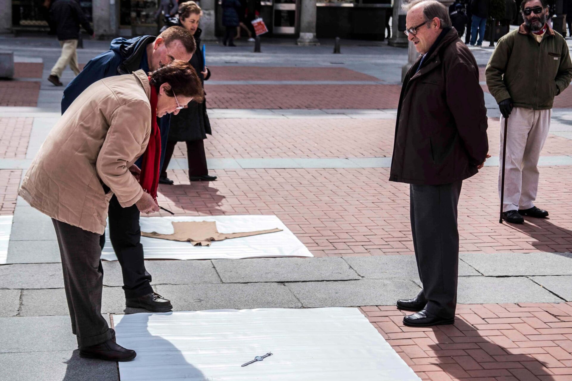 Three people looking at a wristwatch on the white plastic square at Patricia Sandonis large-scale art installation in Plaza Mayor in Valladolid titled Exchange Value