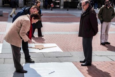 Three people looking at a wristwatch on the white plastic square at Patricia Sandonis large-scale art installation in Plaza Mayor in Valladolid titled Exchange Value