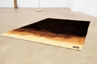 Bleached black and brown towel lying on the floor with a label bearing the phrase “this changes every thought.” A work of art by artist Patricia Sandonis.