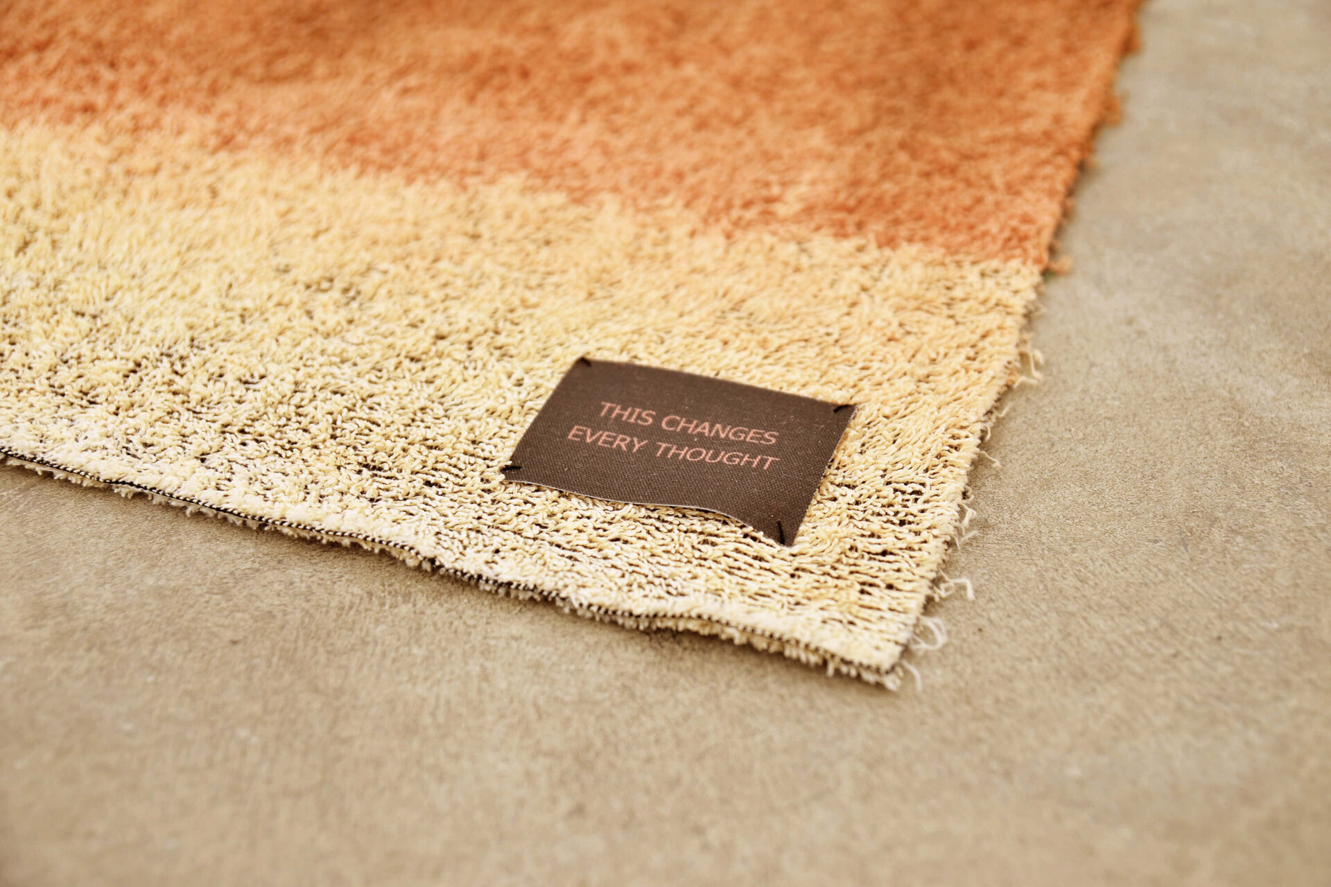 Detail of a brown towel with a label bearing the phrase “this changes every thought.” A work of art by artist Patricia Sandonis.