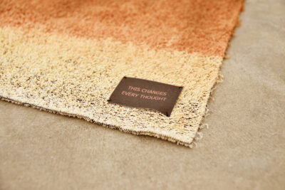 Detail of a brown towel with a label bearing the phrase “this changes every thought.” A work of art by artist Patricia Sandonis.
