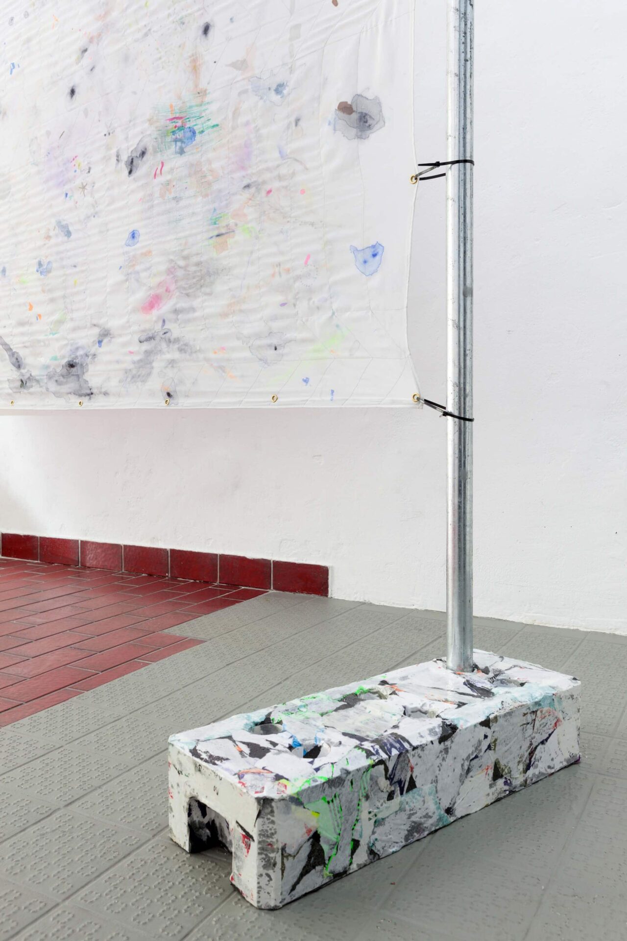 Detail from the artwork Das Kiez Monument showing a white intervened fence foot and a painting of colored fragments on a white surface