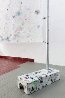 Detail from the artwork Das Kiez Monument showing a white intervened fence foot and a painting of colored fragments on a white surface