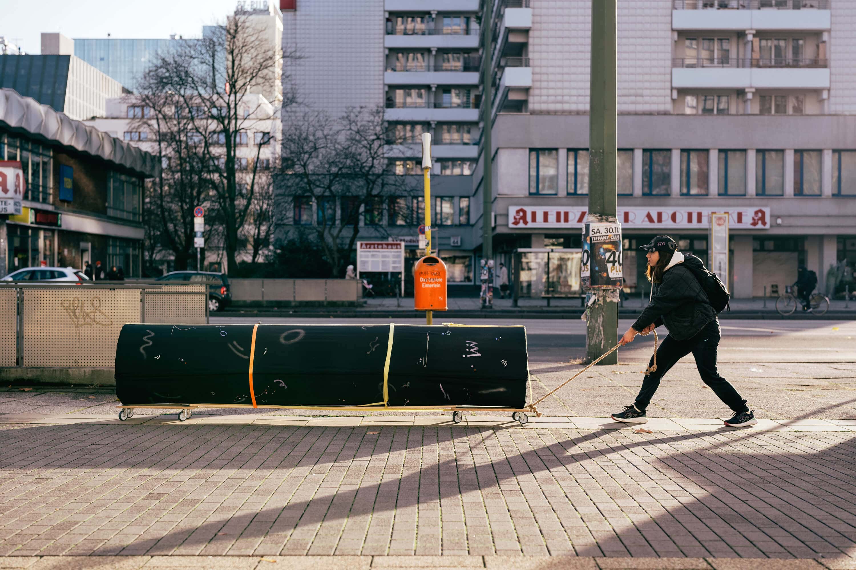 Performance rolling a horizontal black column at Leipziger Straße in Berlin by artist Patricia Sandonis