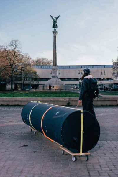 Artist Patricia Sandonis with a black column sculpture called Ignored in Public, looking at the victory column in Mehringplatz in Berlin