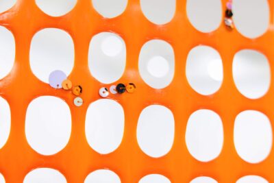 Detail from an artwork by artist Patricia Sandonis showing sequins on an orange security mesh