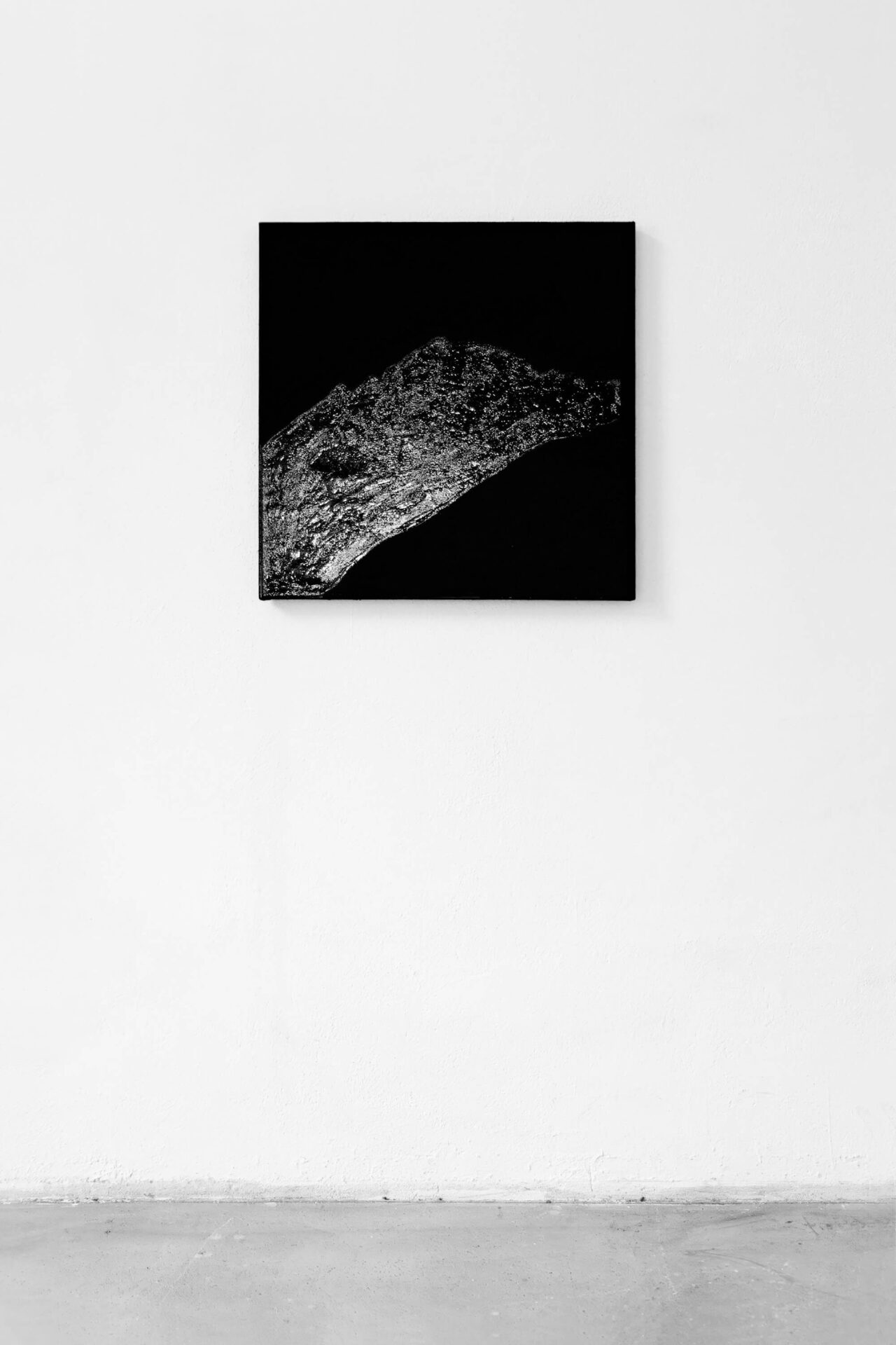 Black square painting hanging on a white wall, reflecting the glossiness of the material