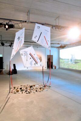 Art Installation of three hand-painted kites hanging and a circle of debris and stones on the floor, a work of art by artist Patricia Sandonis