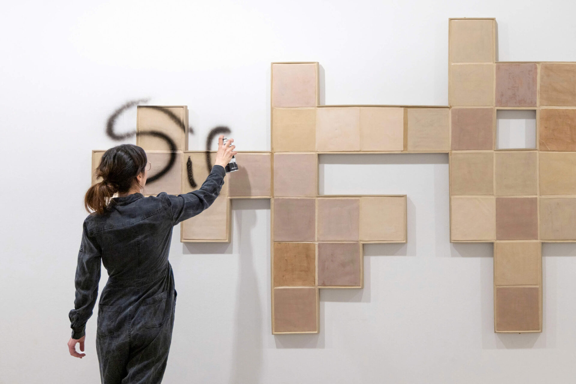 Performance by Patricia Sandonis where the artist writes a message as graffiti over the ceramic tiles of the art installation The In-Between at Museo Patio Herreriano