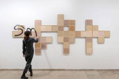 Performance by Patricia Sandonis where the artist writes a message as graffiti over the ceramic tiles of the art installation The In-Between at Museo Patio Herreriano