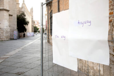 Two street posters hanging on a street fence showing a word. Art Installation by Patricia Sandonis