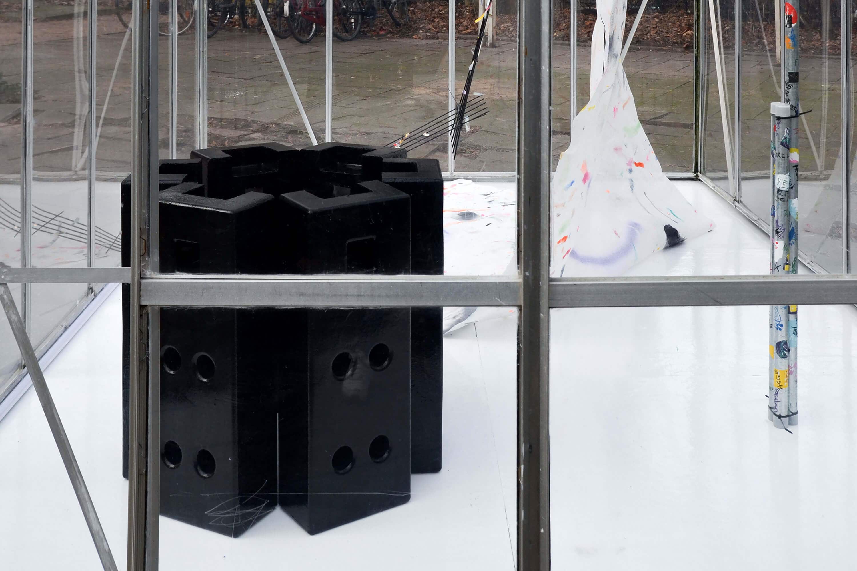Group of black fence feet, placed vertically behind a glass window, an art installation by Patricia Sandonis