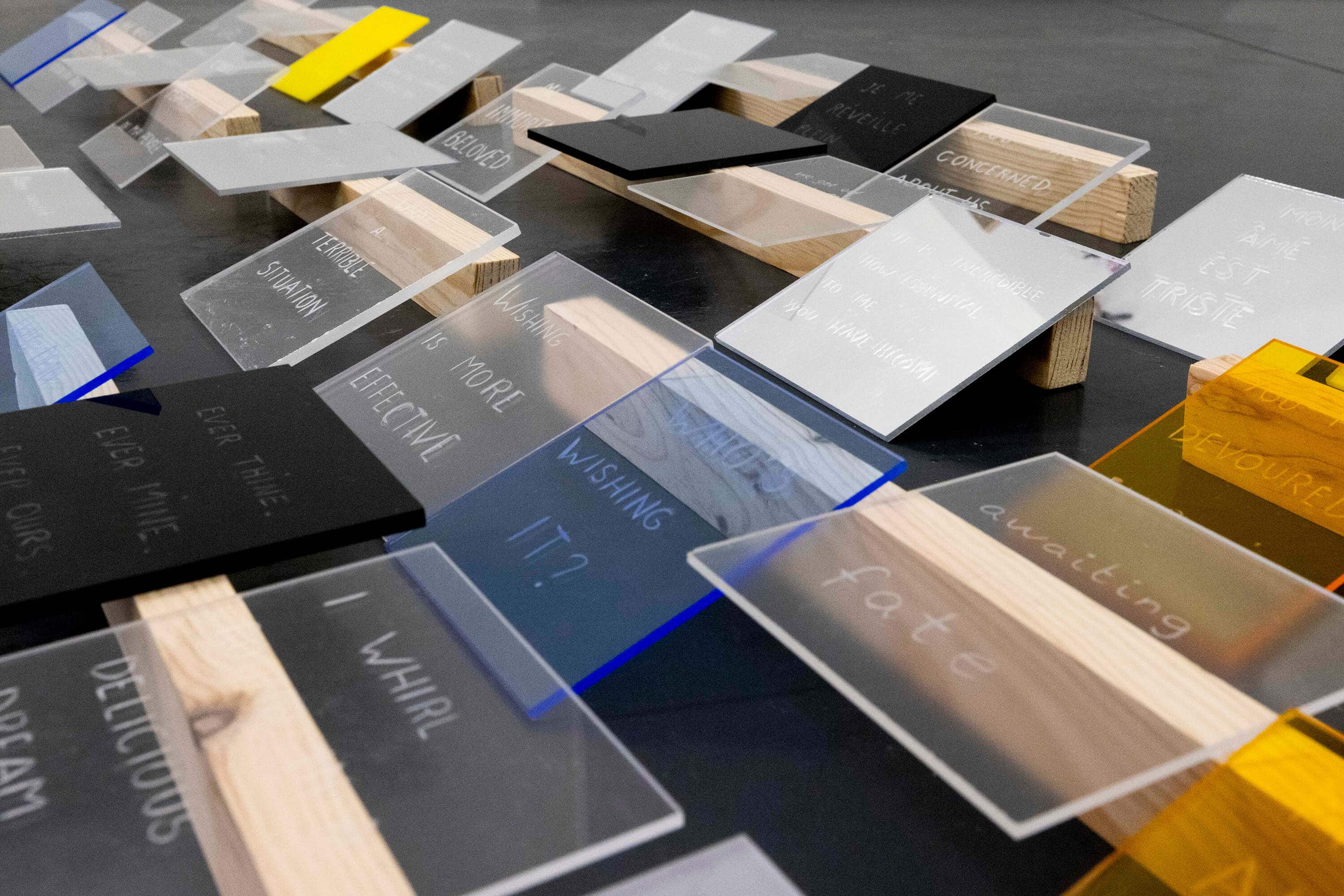 Art installation by artist Patricia Sandonis consisting of methacrylate pieces in different colors engraved with phrases