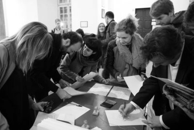 Black and white photography where many people are interacting around a desk with papers and seals