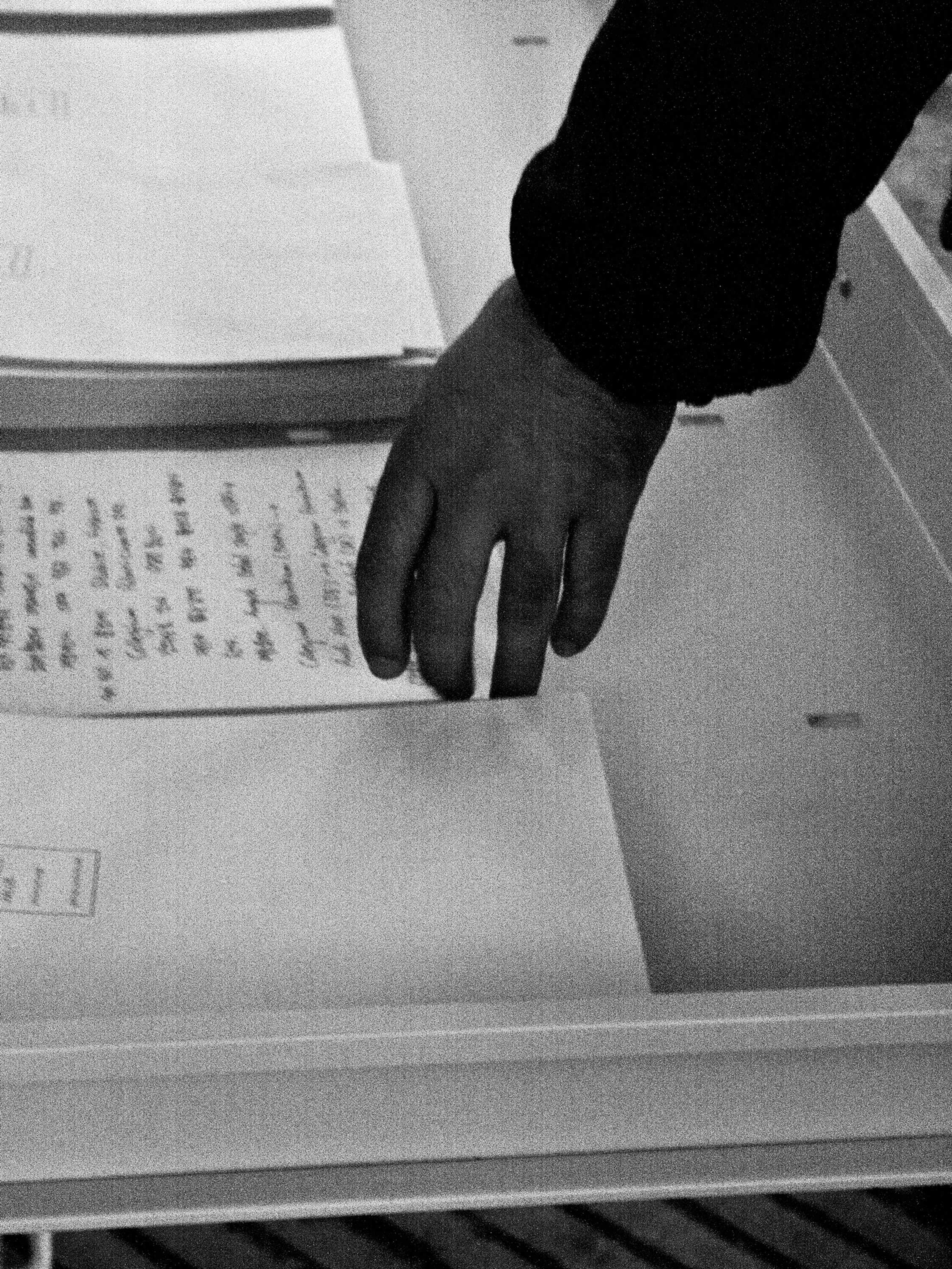 Black and white photography showing a hand picking up a written paper at the art installation titled Exchange Value Intercultural