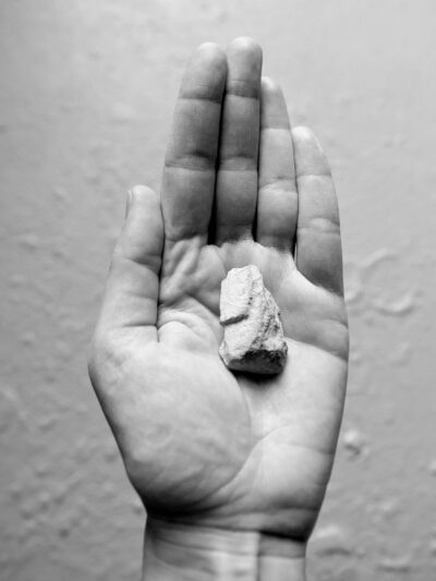 Black and white photography showing a left hand with a small stone
