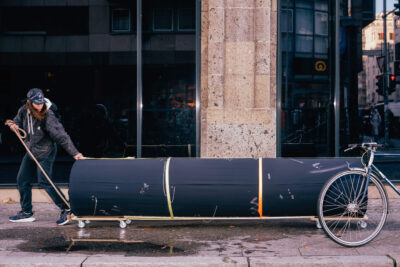 Art performance called Ignored in Public, by artist Patricia Sandonis, moving a horizontal black column through the streets of Berlin
