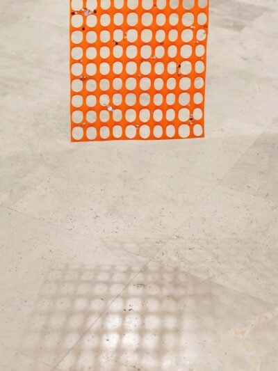 Orange security mesh with sequins hanging on and projecting a shadow on the floor